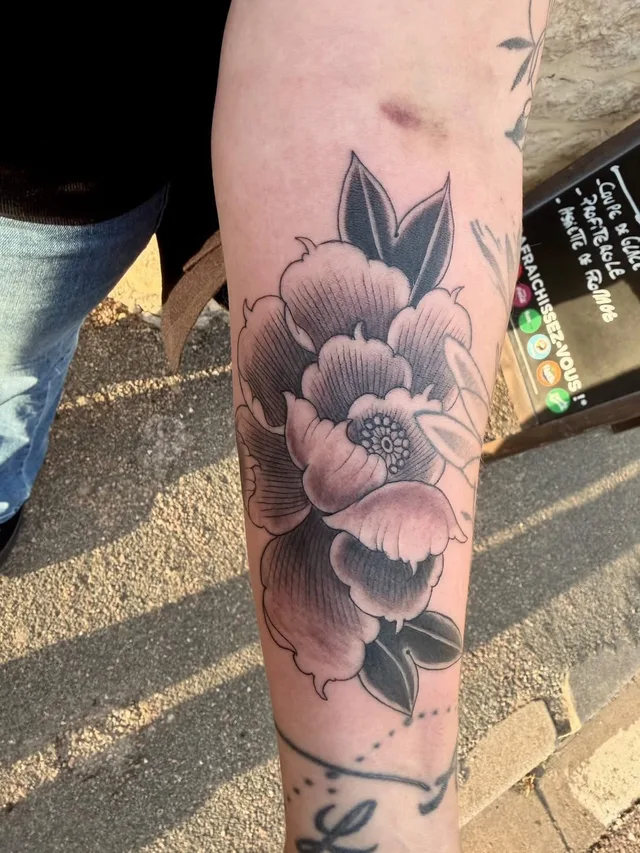 A black and grey peony on a forearm